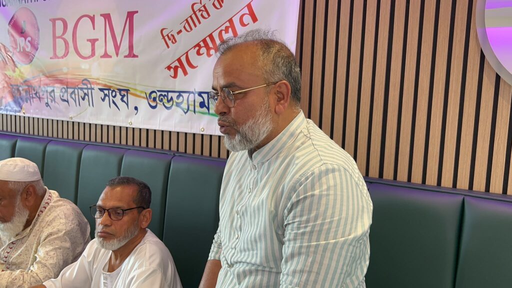 A member in a striped shirt stands and speaks during the Biennial General Meeting, with two colleagues seated beside him.