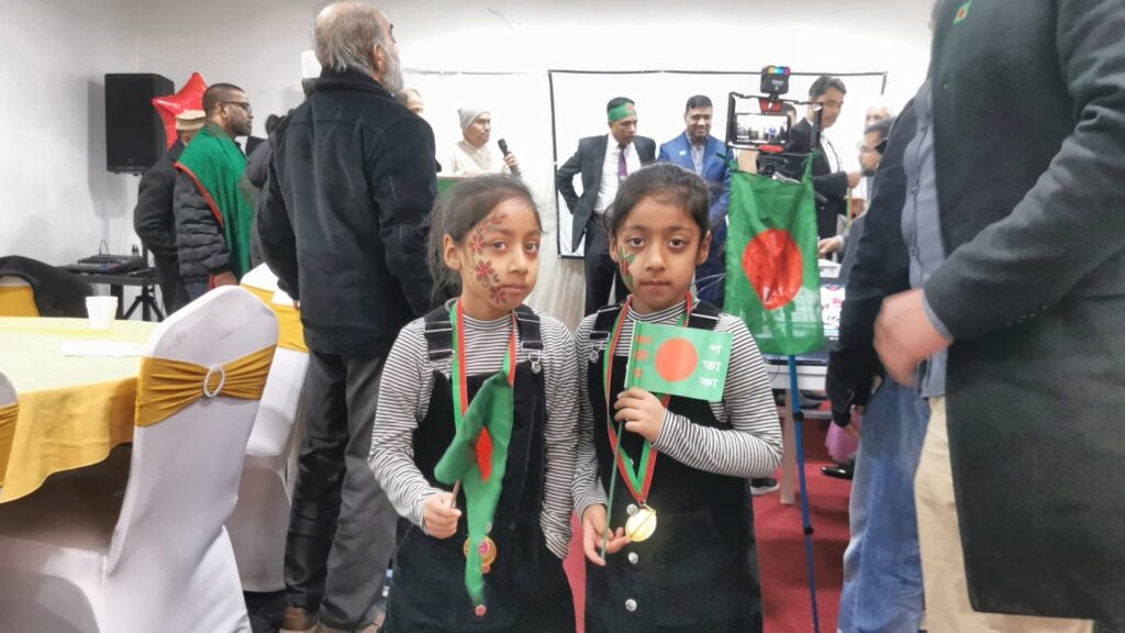 A young child proudly holds the national flag of Bangladesh at the JPS Victory Day celebration.